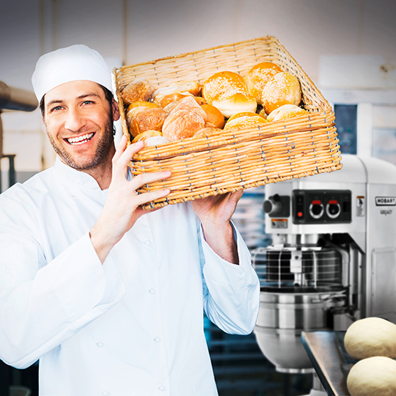 baker holds basket of bread rolls in bakery with hobart mixer